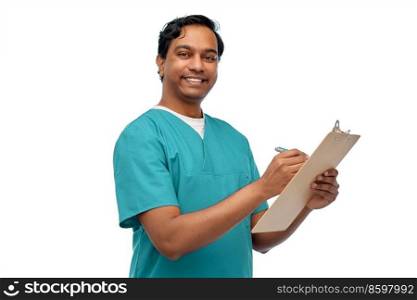 healthcare, profession and medicine concept - happy smiling indian doctor or male nurse in blue uniform writing medical report on clipboard over white background. male doctor writing medical report on clipboard