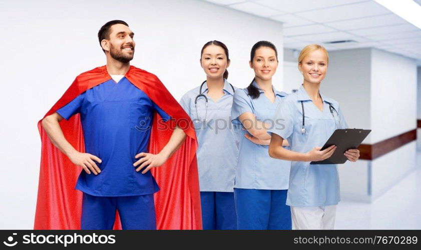 healthcare, profession and medicine concept - happy smiling male doctor in blue uniform and red superhero cape and female nurses over hospital corridor background. male doctor in superhero cape and nurses at clinic