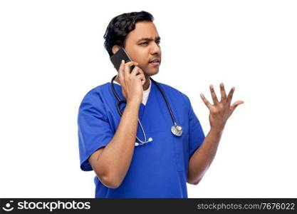 healthcare, profession and medicine concept - indian doctor or male nurse in blue uniform with stethoscope calling on smartphone over white background. indian doctor or male nurse calling on smartphone