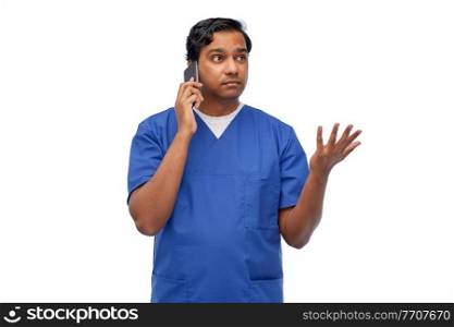 healthcare, profession and medicine concept - indian doctor or male nurse in blue uniform with stethoscope calling on smartphone over white background. indian doctor or male nurse calling on smartphone