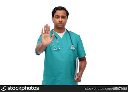 healthcare, profession and medicine concept - indian male doctor in blue uniform with stethoscope and folder showing stop gesture over white background. indian doctor or male nurse showing stop gesture