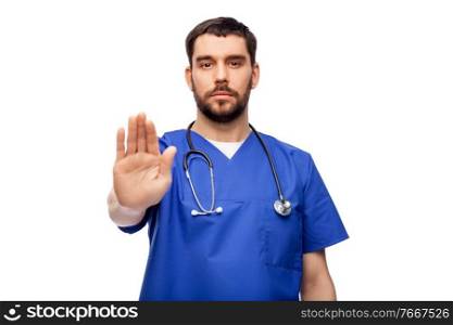 healthcare, profession and medicine concept - male doctor in blue uniform showing stop gesture over white background. doctor or male nurse showing stop gesture