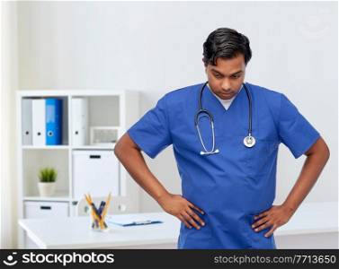 healthcare, profession and medicine concept - stressed indian doctor or male nurse in blue uniform over medical office at hospital background. stressed doctor or male nurse in blue uniform