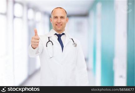 healthcare, profession, gesture and medicine concept - smiling male doctor with stethoscope showing thumbs up over hospital background