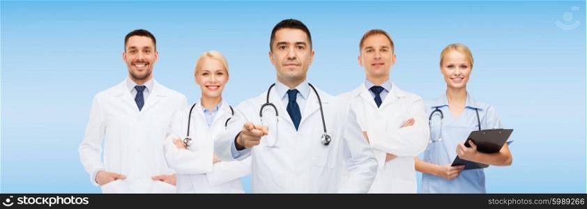 healthcare, profession, gesture, people and medicine concept - group of doctors with stethoscopes and clipboard pointing at you over blue background