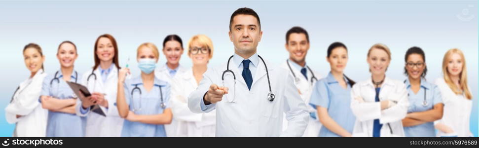 healthcare, profession, gesture, people and medicine concept - international group of doctors with stethoscopes and clipboard pointing at you over gray background