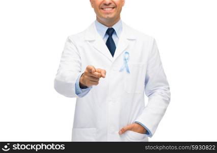 healthcare, profession, people and medicine concept - close up of smiling male doctor in white coat with sky blue prostate cancer awareness ribbon pointing finger to you