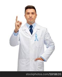 healthcare, profession, people and medicine concept - male doctor in white coat with sky blue prostate cancer awareness ribbon pointing finger up