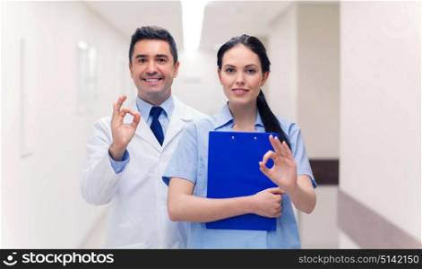 healthcare, profession, people and medicine concept - smiling doctor and nurse with clipboard showing ok hand sign at hospital. doctor and nurse showing ok sign at hospital