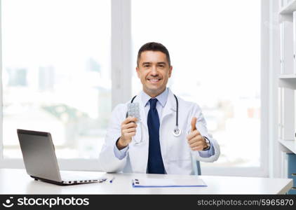 healthcare, profession, people and medicine concept - smiling male doctor in white coat with tablets and laptop computer showing thumbs up in medical office