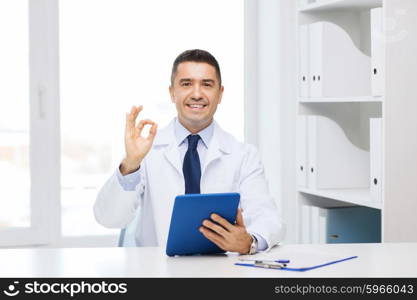 healthcare, profession, people and medicine concept - smiling male doctor in white coat with tablet pc computer showing ok hand sign in medical office