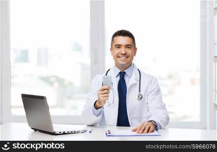 healthcare, profession, people and medicine concept - smiling male doctor in white coat with tablets and laptop computer in medical office