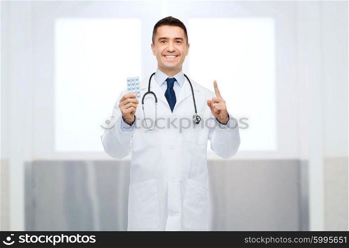 healthcare, profession, people and medicine concept - smiling male doctor in white coat with pills pointing his finger up