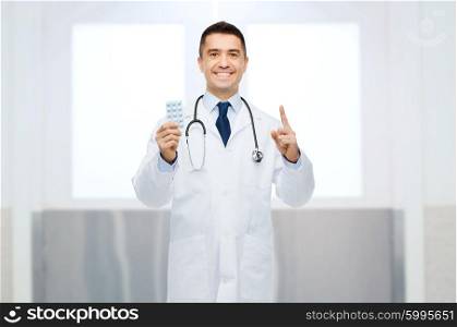 healthcare, profession, people and medicine concept - smiling male doctor in white coat with pills pointing his finger up