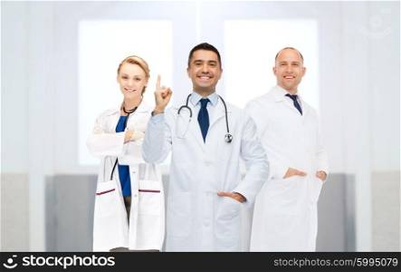healthcare, profession, people, gesture and medicine concept - group of happy doctors at hospital pointing finger up