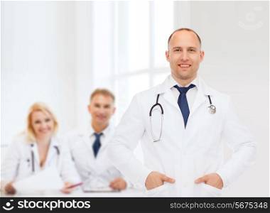 healthcare, profession, teamwork, people and medicine concept - smiling male doctor with stethoscope in white coat over over group of medics