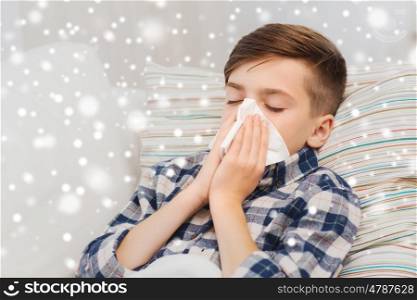 healthcare, rhinitis, people and medicine concept - ill boy with flu lying in bed and blowing his nose at home over snow