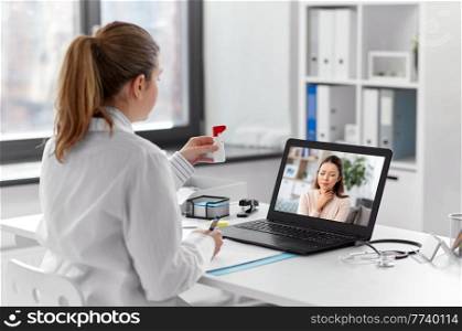 healthcare, technology and medicine concept - female doctor having video call with sick woman patient on laptop computer at hospital and showing oral spray. doctor having video call with patient on laptop