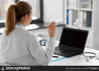 healthcare, technology and medicine concept - female doctor in white coat with laptop computer having video call and waving hand at hospital. doctor with laptop having video call at hospital