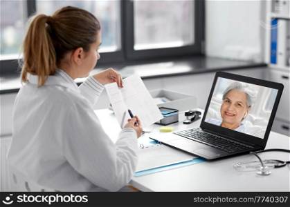 healthcare, technology and medicine concept - female doctor in white coat with laptop computer and cardiogram having video call with patient at hospital. doctor with laptop having video call at hospital
