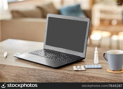 healthcare, technology and medicine concept - laptop computer, drugs and cup on table at home. laptop computer, drugs and cup on table at home