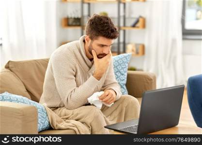 healthcare, technology and medicine concept - sick man in blanket having video call on laptop computer at home. sick man having video call on laptop at home