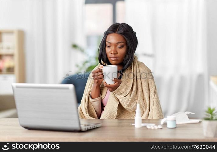 healthcare, technology and people concept - african american sick woman in blanket with tea cup having video call on laptop computer at home. sick woman with tea having video call on laptop