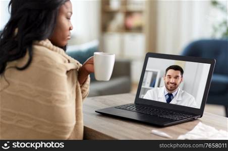 healthcare, technology and people concept - african american sick woman in blanket having video call or online consultation with smiling doctor on laptop computer at home. sick woman having video call with doctor on laptop