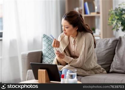 healthcare, technology and people concept - sick asian woman in blanket with medicine having video call on tablet pc computer at home. sick woman with medicine has video consultation