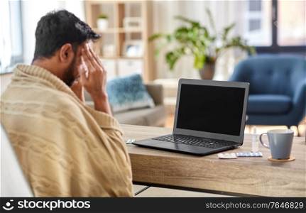 healthcare, technology and people concept - sick indian man in blanket having video call on laptop computer at home. sick indian man having video call on laptop