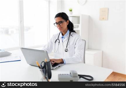 healthcare, technology people and medicine concept - female doctor in white coat and glasses typing on laptop computer at hospital. female doctor typing on laptop at hospital