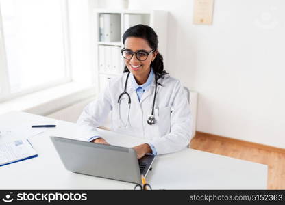 healthcare, technology people and medicine concept - happy smiling female doctor in white coat and glasses typing on laptop computer at hospital. happy female doctor typing on laptop at hospital