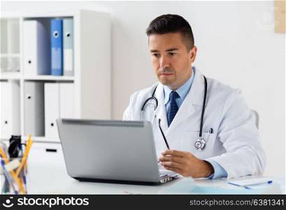 healthcare, technology, people and medicine concept - male doctor in white coat with laptop computer in hospital. male doctor in white coat with laptop at hospital
