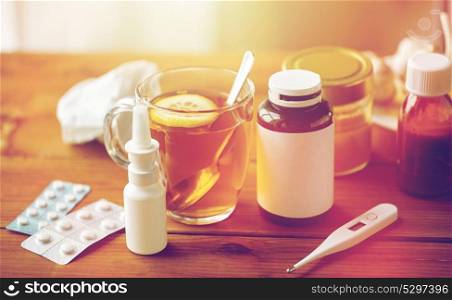 healthcare, traditional medicine and flu concept - cup of tea with lemon, thermometer and drugs on wooden table. traditional medicine and drugs
