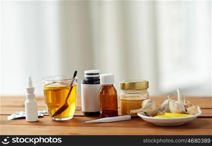 healthcare, traditional medicine and flu concept - drugs, thermometer, honey and cup of tea on wooden table