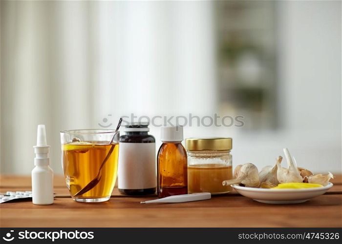 healthcare, traditional medicine and flu concept - drugs, thermometer, honey and cup of tea on wooden table