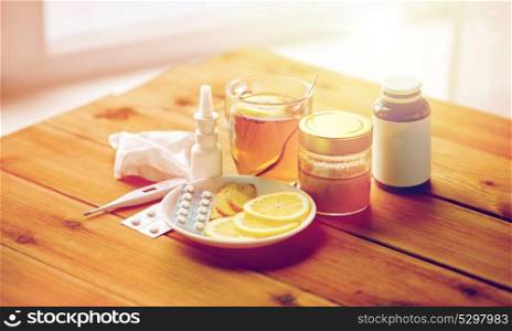 healthcare, traditional medicine and flu concept - drugs, thermometer, honey and cup of tea on wooden table. drugs, thermometer, honey and cup of tea on wood