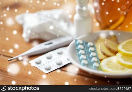 healthcare, traditional medicine and flu concept - tea cup with lemon, ginger, honey and pills on wooden table over snow. traditional medicine and drugs
