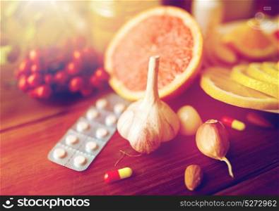 healthcare, traditional medicine, flu and ethnoscience concept - garlic and pills on wooden table. traditional medicine and drugs