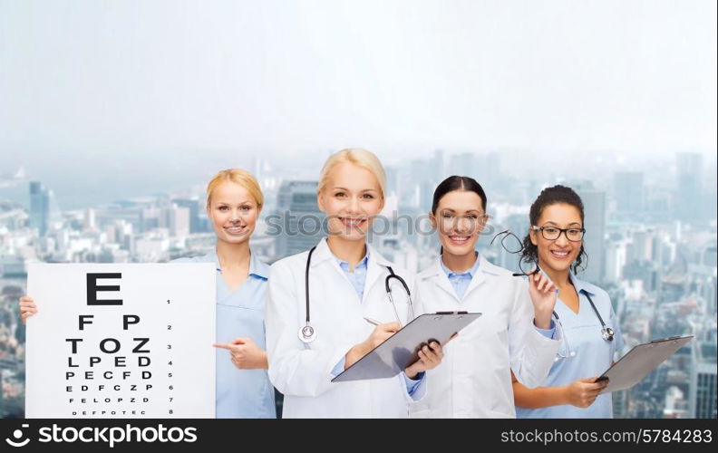 healthcare, vision and medicine concept - smiling female eye doctors and nurses with eye exam chart, glasses and clipboard