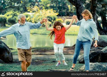 Healthy active father and mother in the park grabbing and playing with daughter child on weekend in summer. Active senior and family lifestyle concept.
