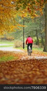 Healthy active lifestyle, cycling outdoors man exercising with bicycle riding a bike, golden autumn fall leaves in park