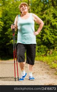 Healthy active retirement concept. Senior woman practicing nordic walking in forest park. Elderly female enjoying nature fresh air. Senior woman practicing nordic walking in park