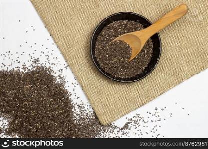 Healthy and diet food, Chia seeds in black bowl on linen cloth and heap over white background.