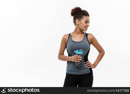 Healthy and Fitness concept - beautiful African American girl in sport clothes holding water bottle after workout. Isolated on white studio background.. Healthy and Fitness concept - beautiful African American girl in sport clothes holding water bottle after workout. Isolated on white studio background