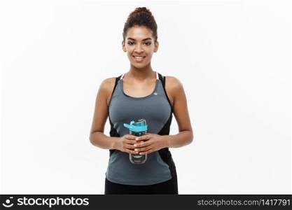 Healthy and Fitness concept - beautiful African American girl in sport clothes holding water bottle after workout. Isolated on white studio background.. Healthy and Fitness concept - beautiful African American girl in sport clothes holding water bottle after workout. Isolated on white studio background