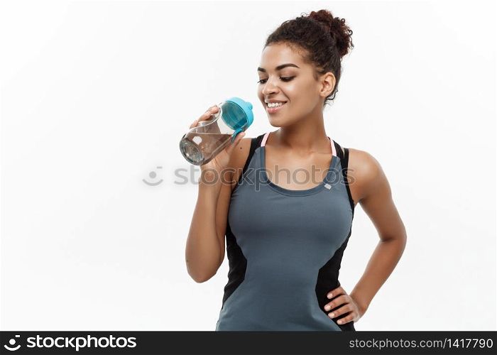 Healthy and Fitness concept - beautiful African American girl in sport clothes drinking water after workout. Isolated on white studio background.. Healthy and Fitness concept - beautiful African American girl in sport clothes drinking water after workout. Isolated on white studio background