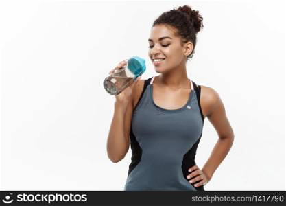 Healthy and Fitness concept - beautiful African American girl in sport clothes drinking water after workout. Isolated on white studio background.. Healthy and Fitness concept - beautiful African American girl in sport clothes drinking water after workout. Isolated on white studio background