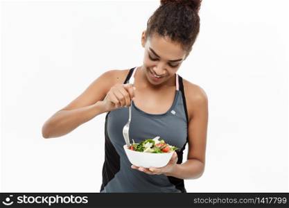 Healthy and Fitness concept - Beautiful American African lady in fitness clothes on diet eating fresh salad. Isolated on white background. Healthy and Fitness concept - Beautiful American African lady in fitness clothes on diet eating fresh salad. Isolated on white background.