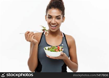 Healthy and Fitness concept - Beautiful American African lady in fitness clothes on diet eating fresh salad. Isolated on white background. Healthy and Fitness concept - Beautiful American African lady in fitness clothes on diet eating fresh salad. Isolated on white background.